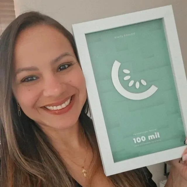 Patrícia, criadora do Curso Bonequinhas 3D, segurando o prêmio Kiwify Emerald de 100 mil reais em vendas
